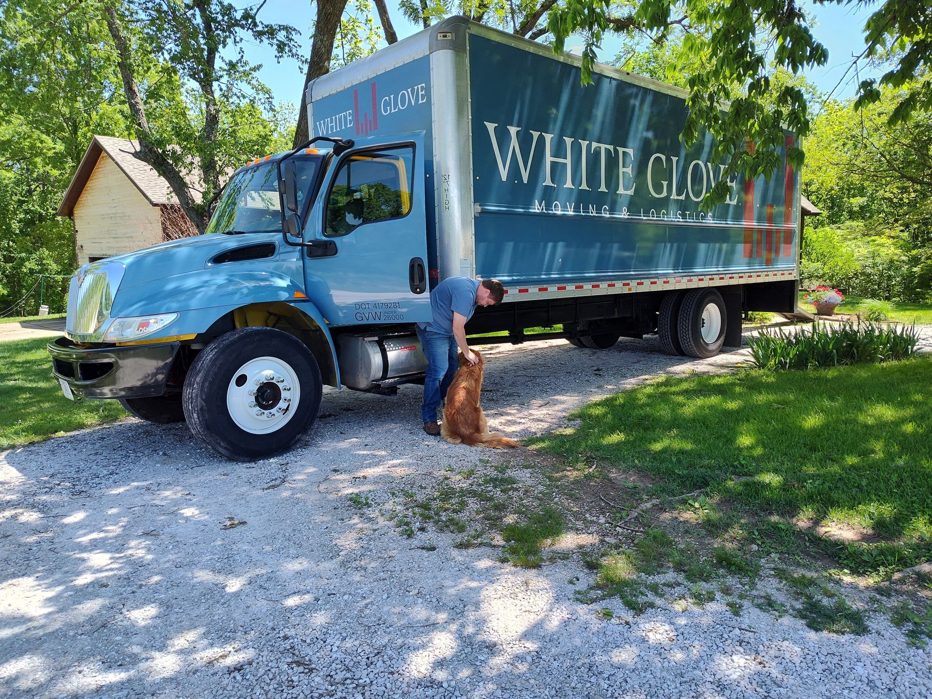 White Goose delivery truck parked on a gravel driveway beside a small dog and a house