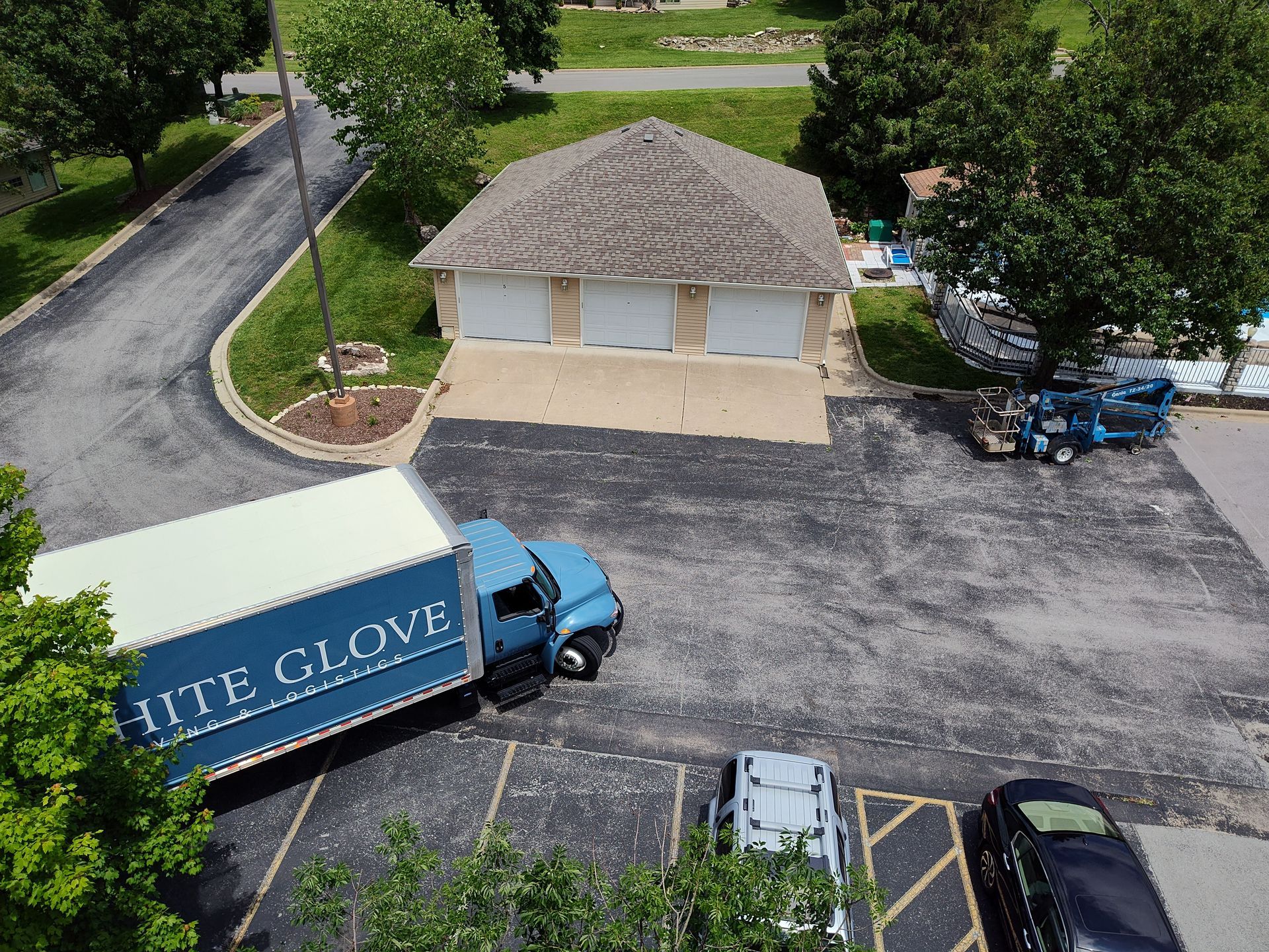 Blue truck with white trailer parked by a beige building in a lot with trees and other cars.