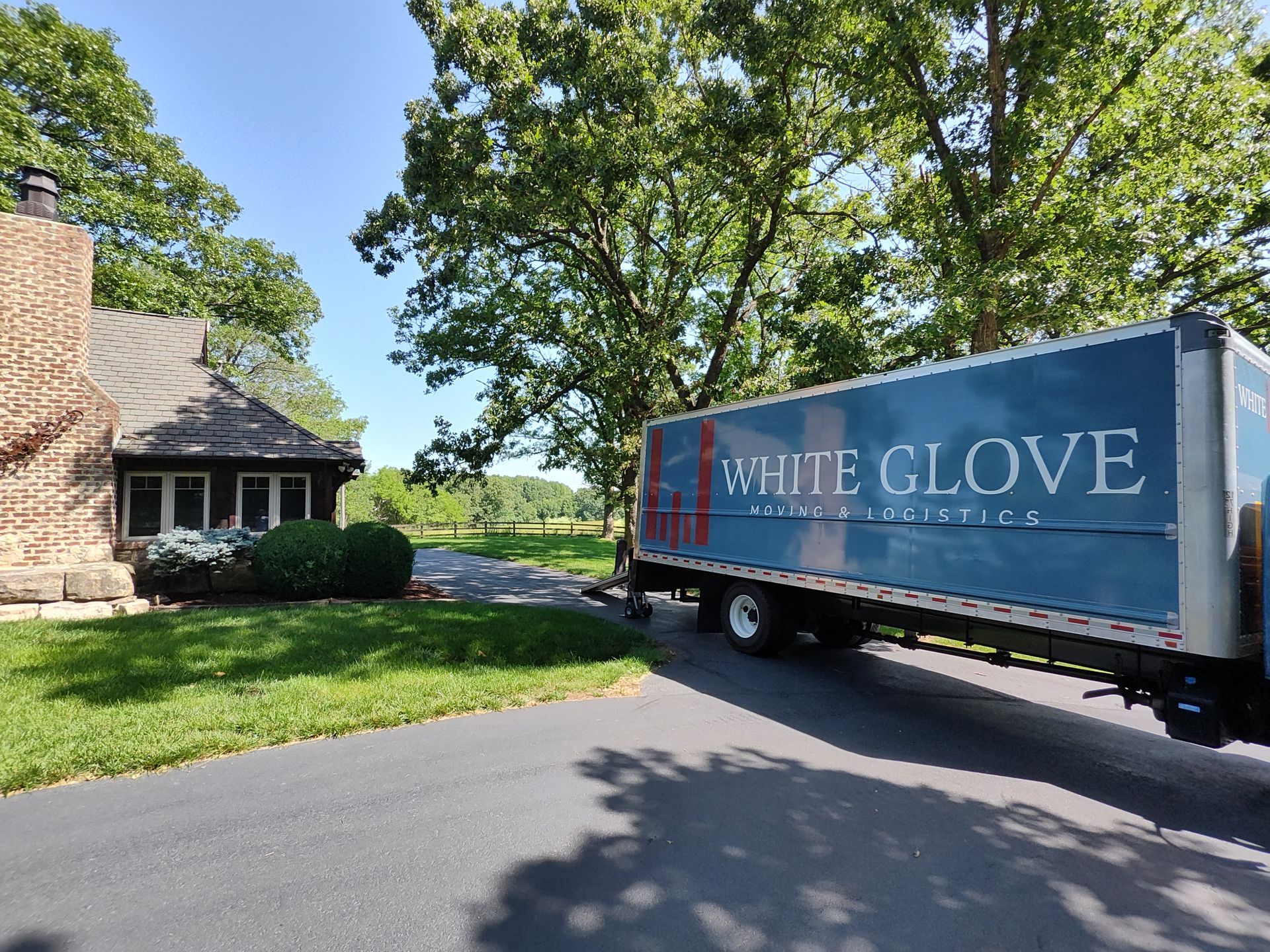 Blue HERIE CLOVE truck parked on a driveway beside a house and trees on a sunny day