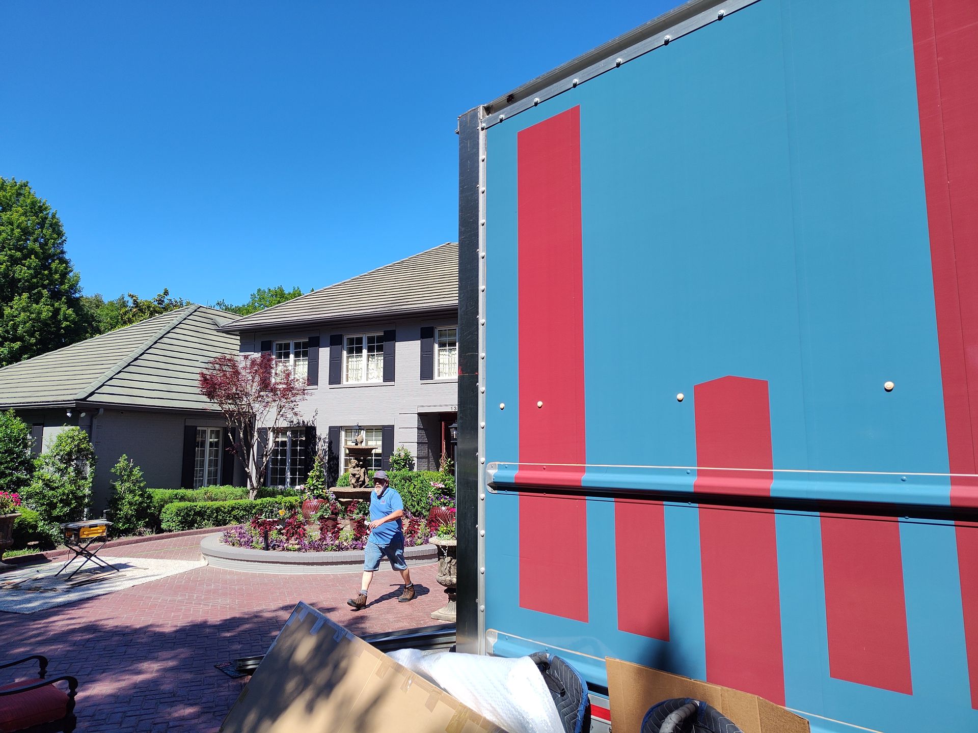 Blue and red truck or container blocking view of a courtyard with a house and landscaping