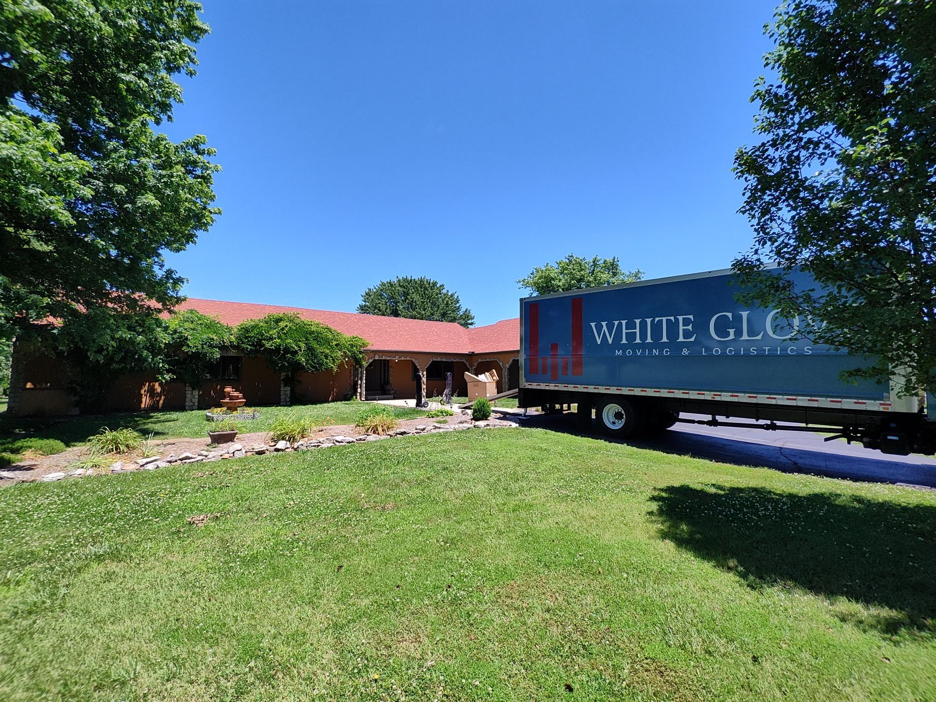 Brick building with red roof, green lawn, and a White Glove truck parked outside on a sunny day