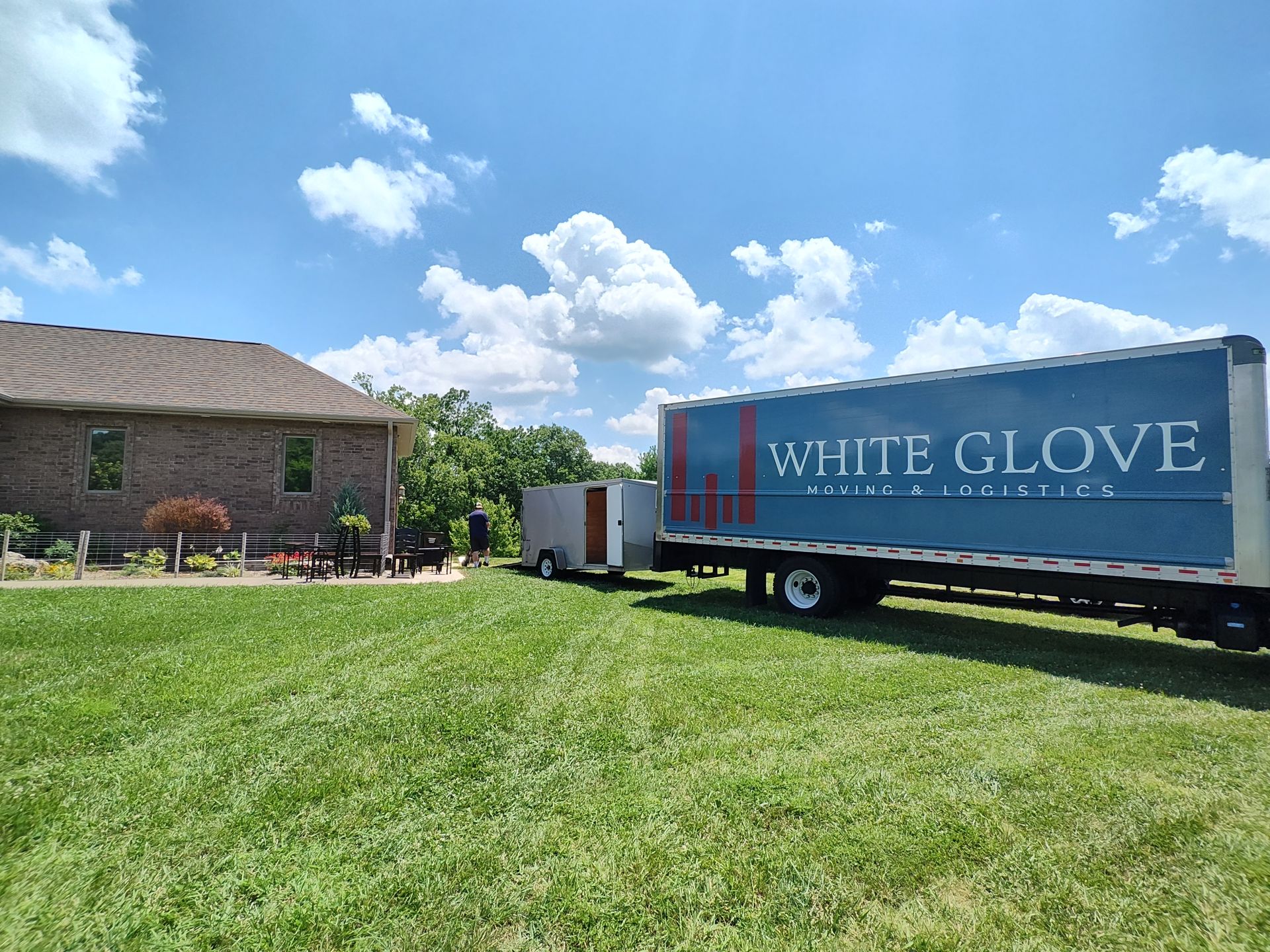 Blue White Glove moving truck parked on a grassy lawn beside a brick building under a sunny sky