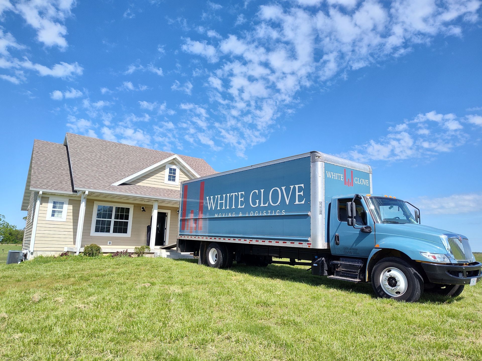 Blue delivery truck parked beside a beige house under a bright blue sky.