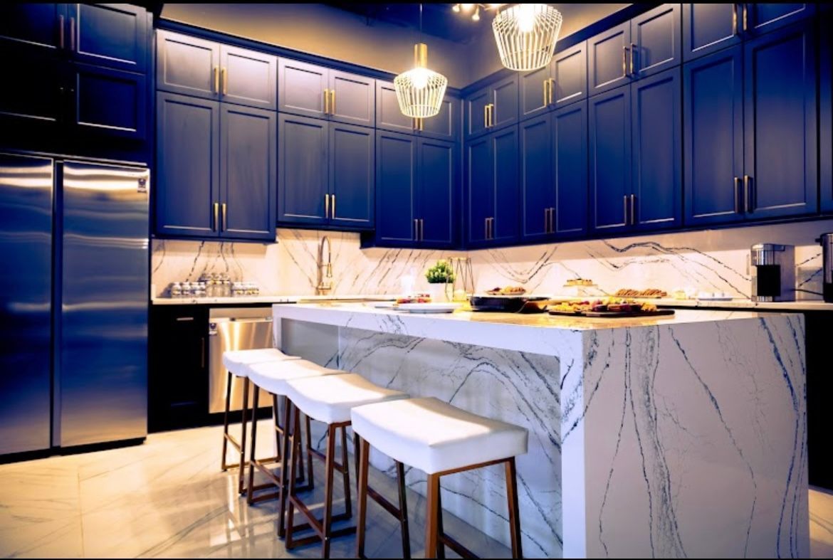 Modern kitchen with navy blue cabinets, marble countertops, stainless steel appliances, and island with white stools.