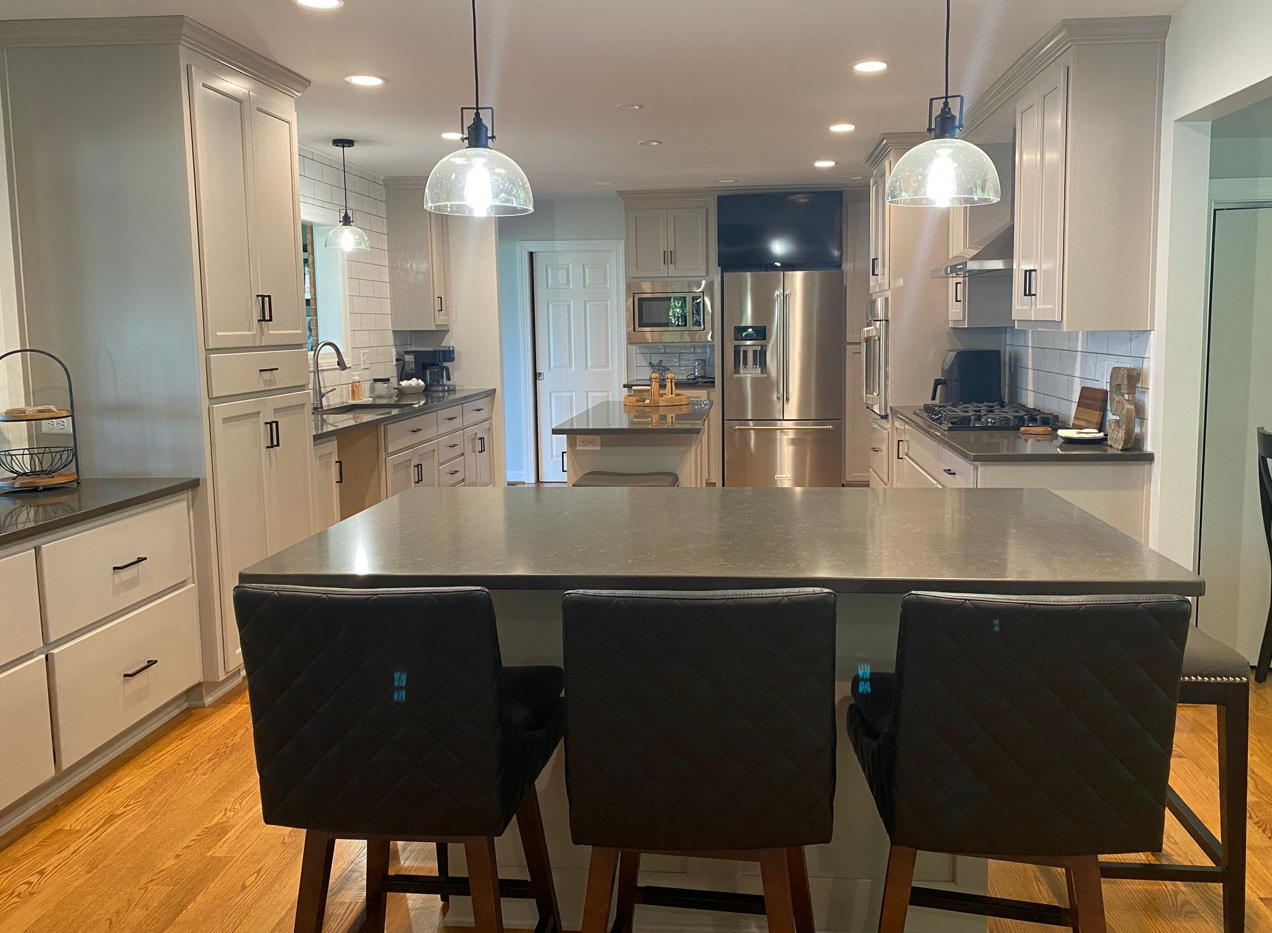 Modern kitchen with island and three bar stools, light cabinets, stainless steel appliances, and wood floors.