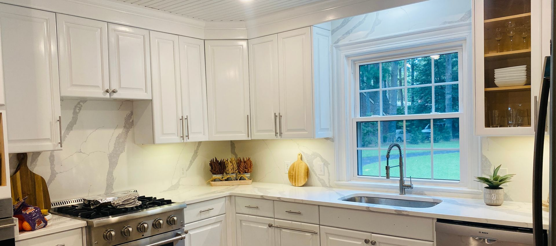 White kitchen with marble countertops, stainless steel appliances, and a window over the sink.