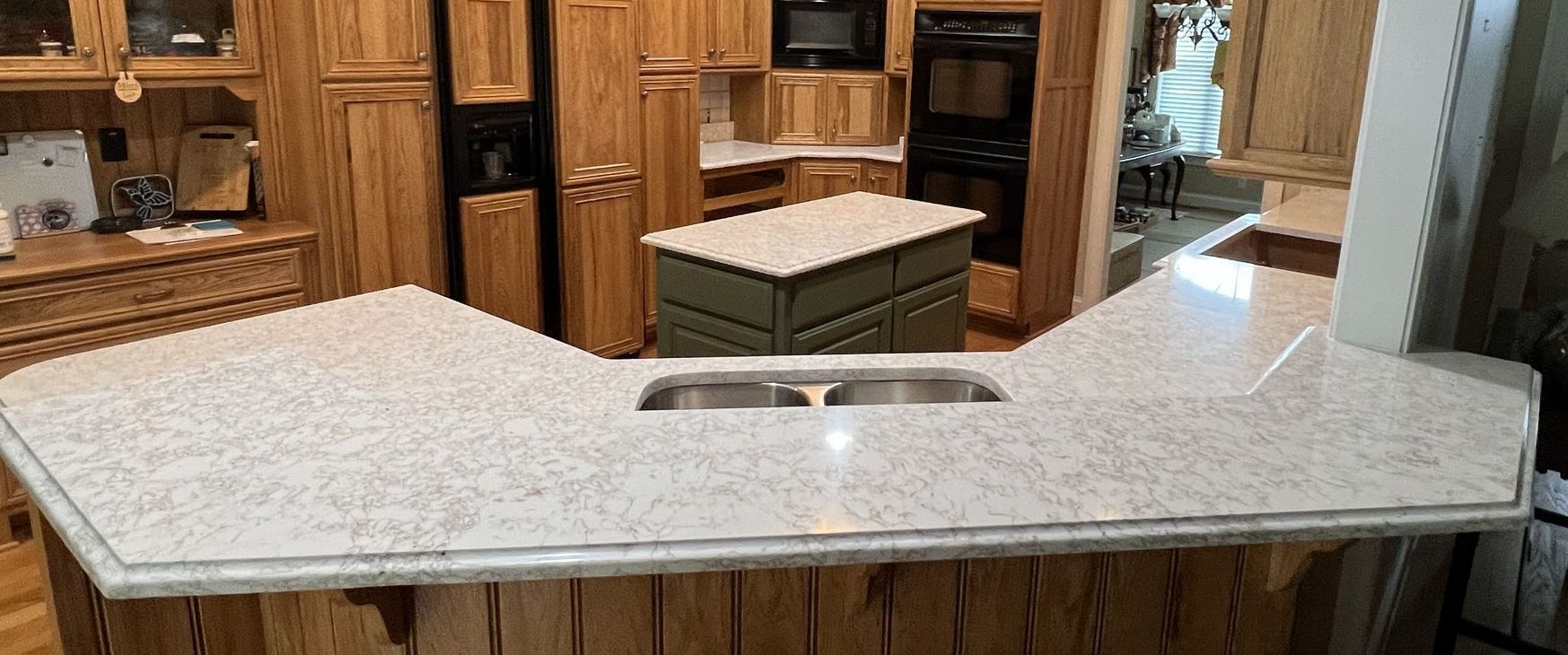 Kitchen with light speckled countertops and wooden cabinets. Island and sink are visible.