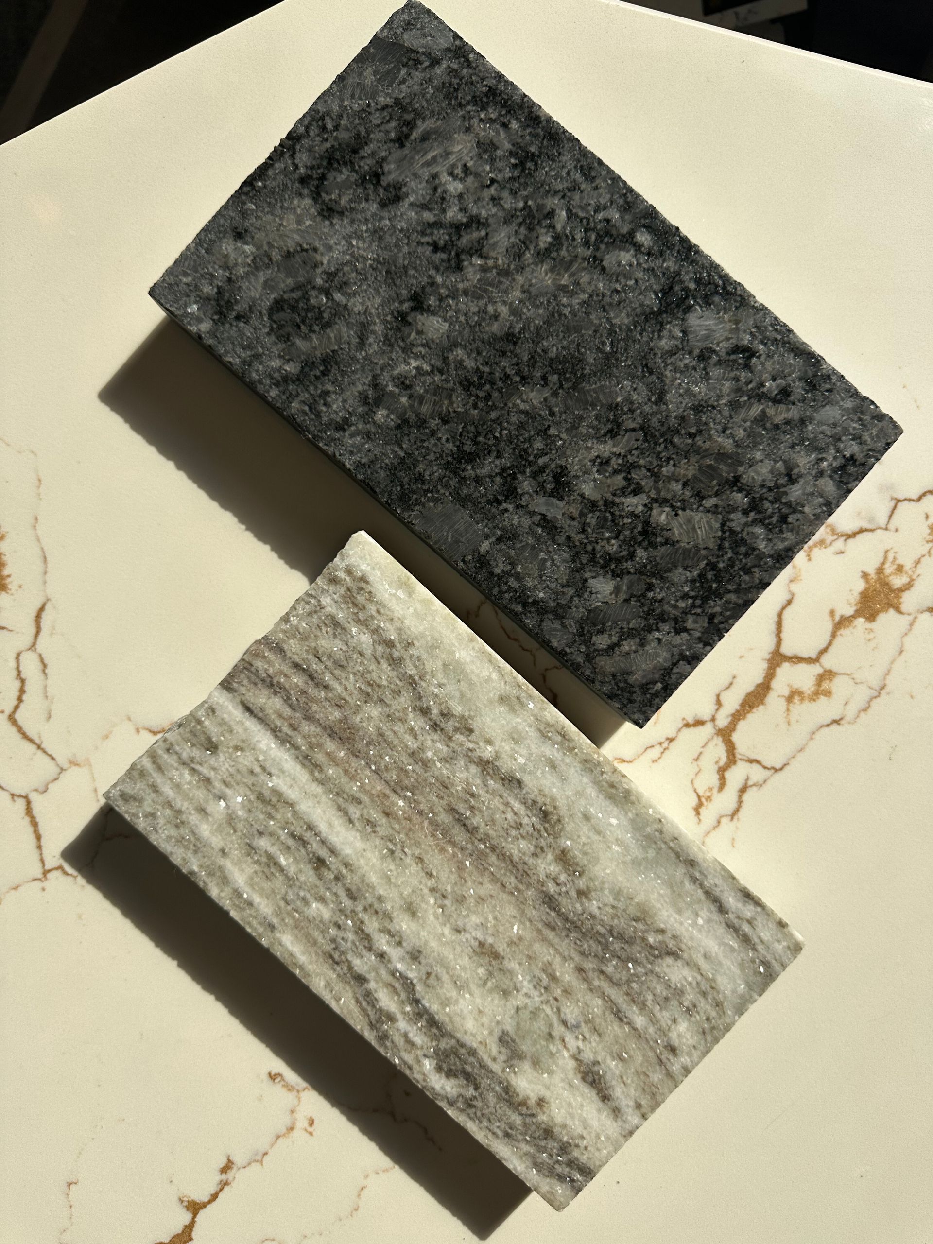 Two stone samples: dark speckled gray granite and light marble with brown veining, on a cream-colored surface.