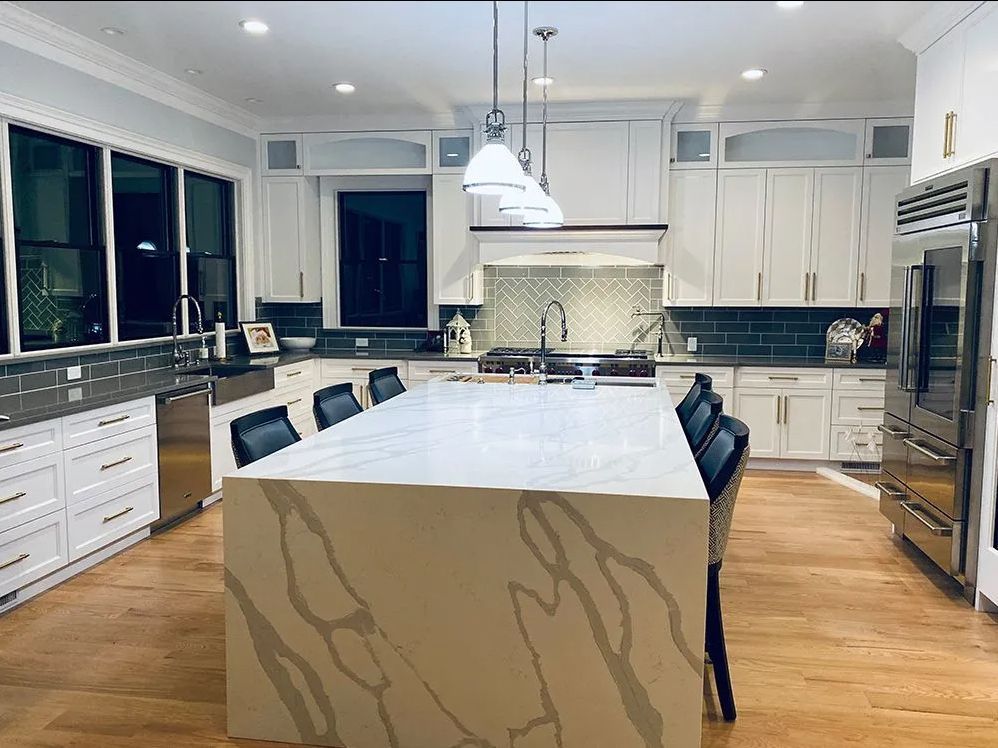 Spacious white kitchen with island, wood floors, and stainless steel appliances.