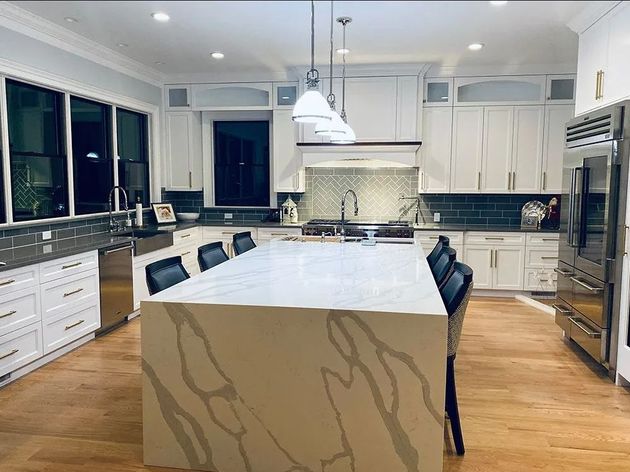 Spacious white kitchen with island, wood floors, and stainless steel appliances.