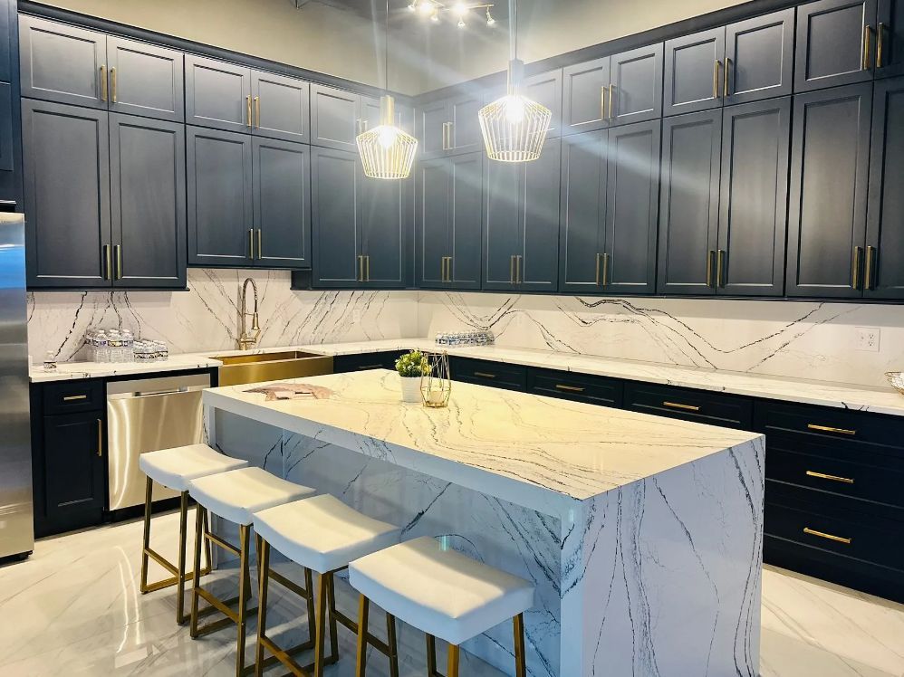 Dark blue kitchen with gold hardware, white countertops, and an island with stools.