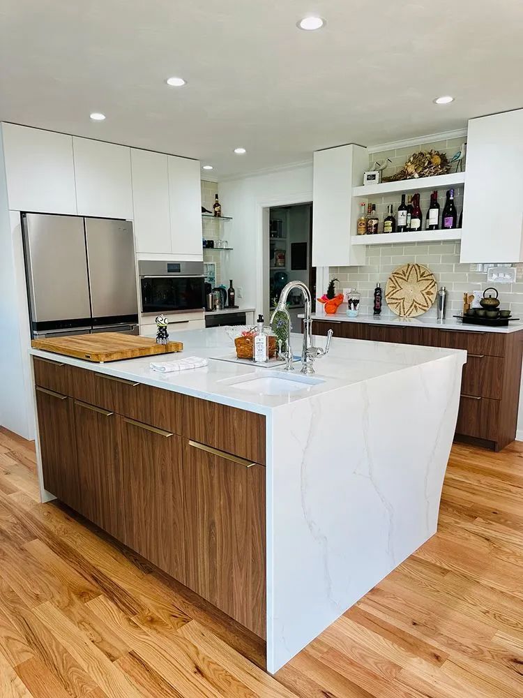 Modern kitchen with white countertops, brown cabinetry, island, stainless steel appliances, and wooden floor.