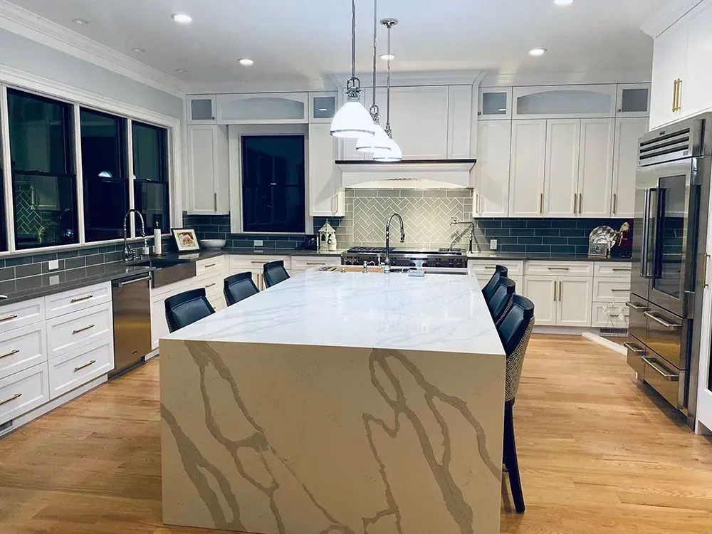 Bright white modern kitchen with a large marble island, pendant lights, and hardwood floors