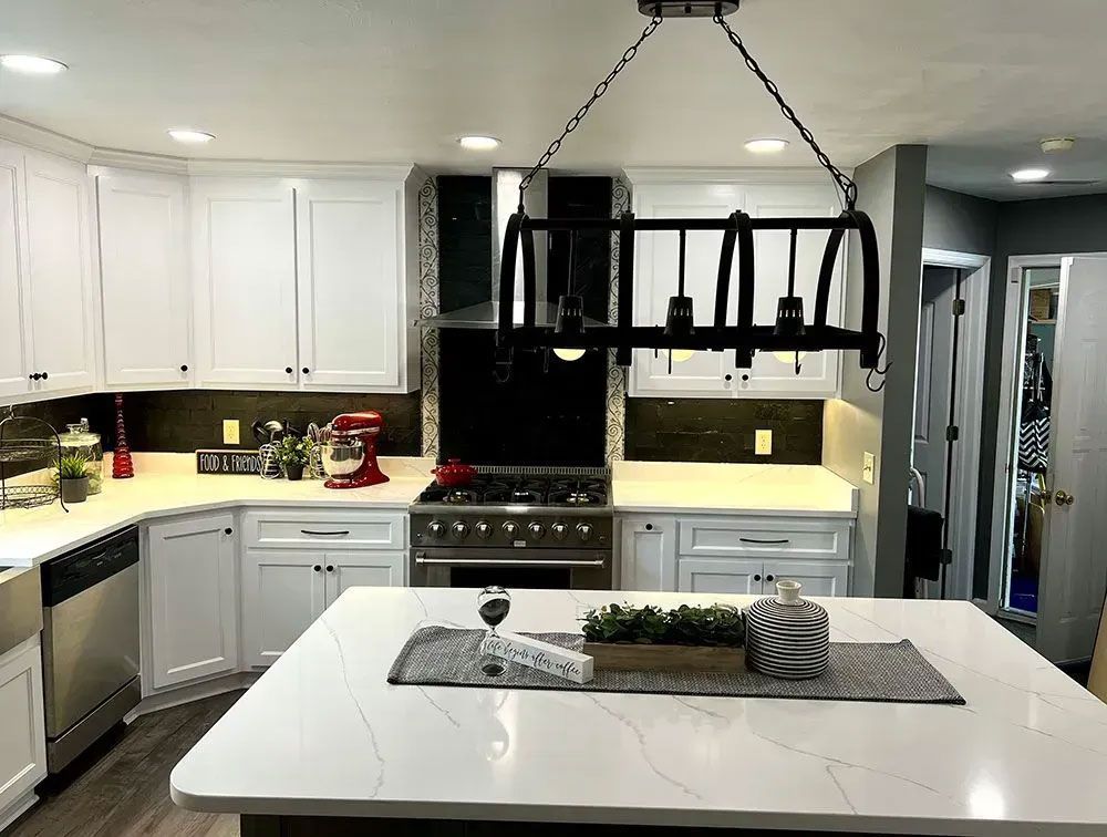 Modern white kitchen with island, black pendant light, stainless stove, and bright under-cabinet lighting.
