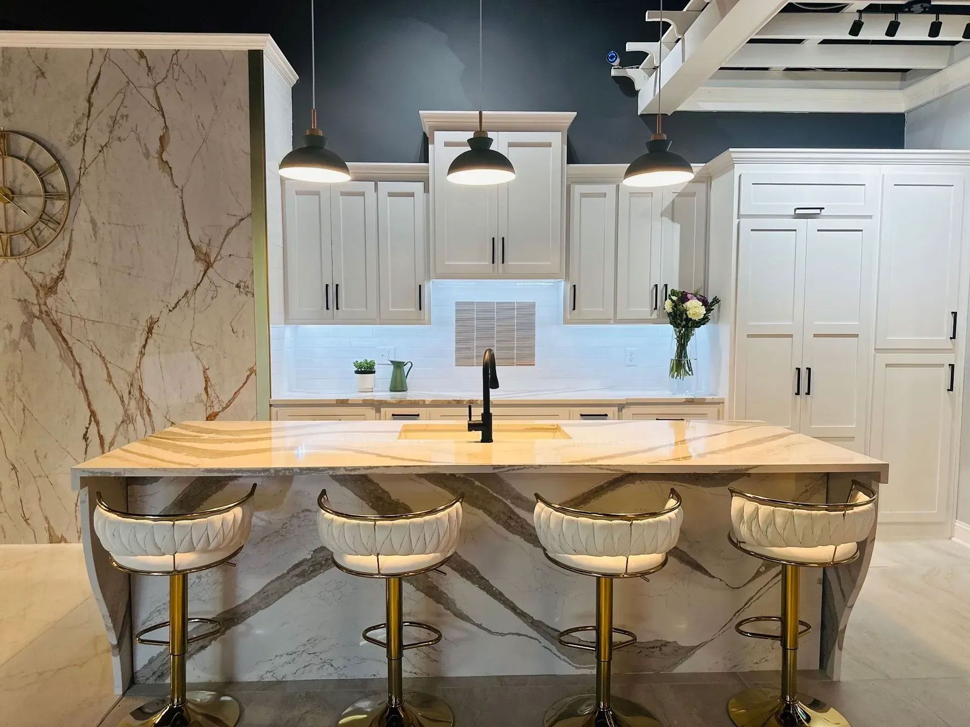 Modern kitchen with marble island, three stools, white cabinets, and pendant lights.