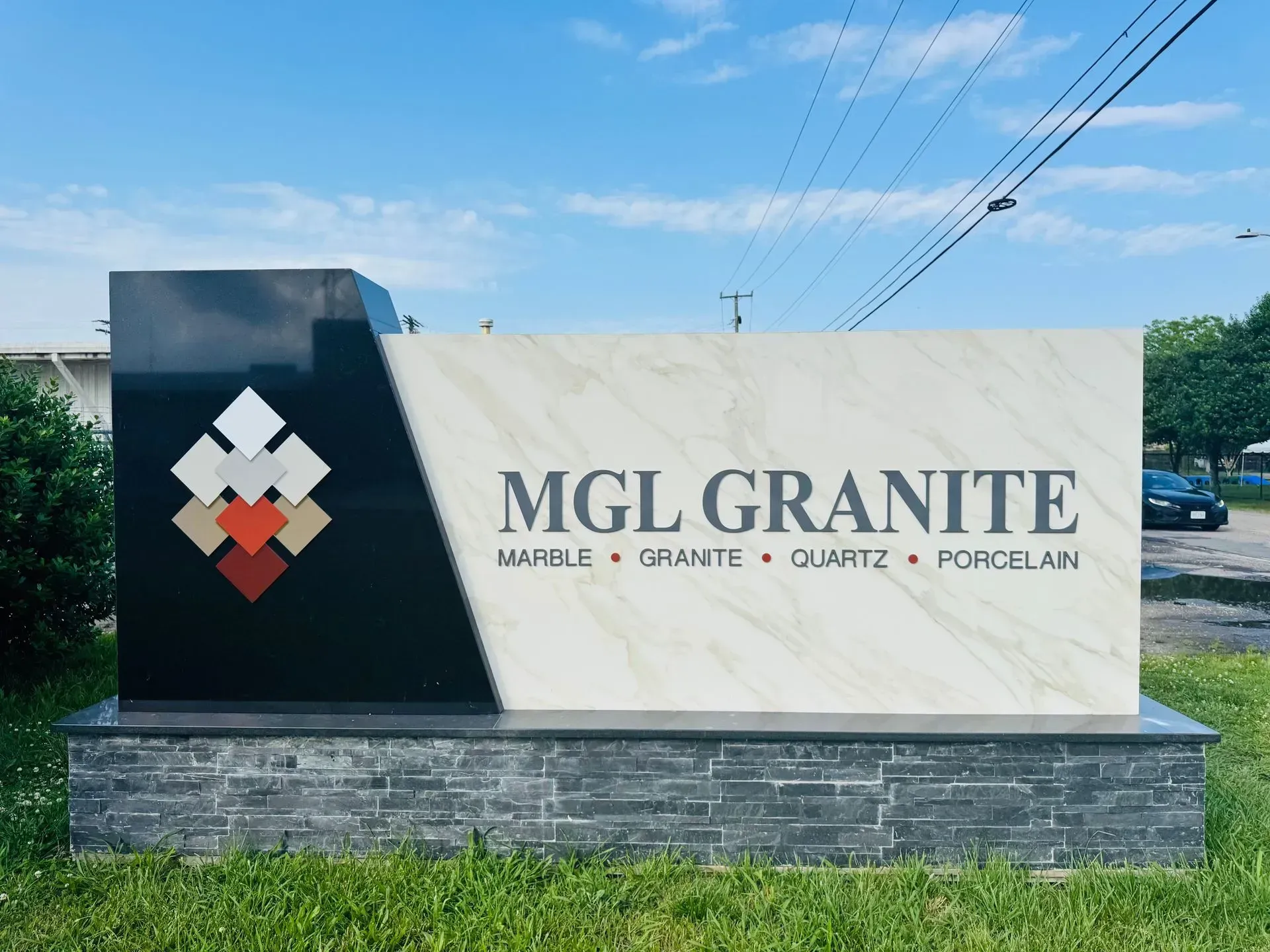 Sign for MGL Granite, marble, granite, quartz, and porcelain retailer. Features logo and business name on stone display.