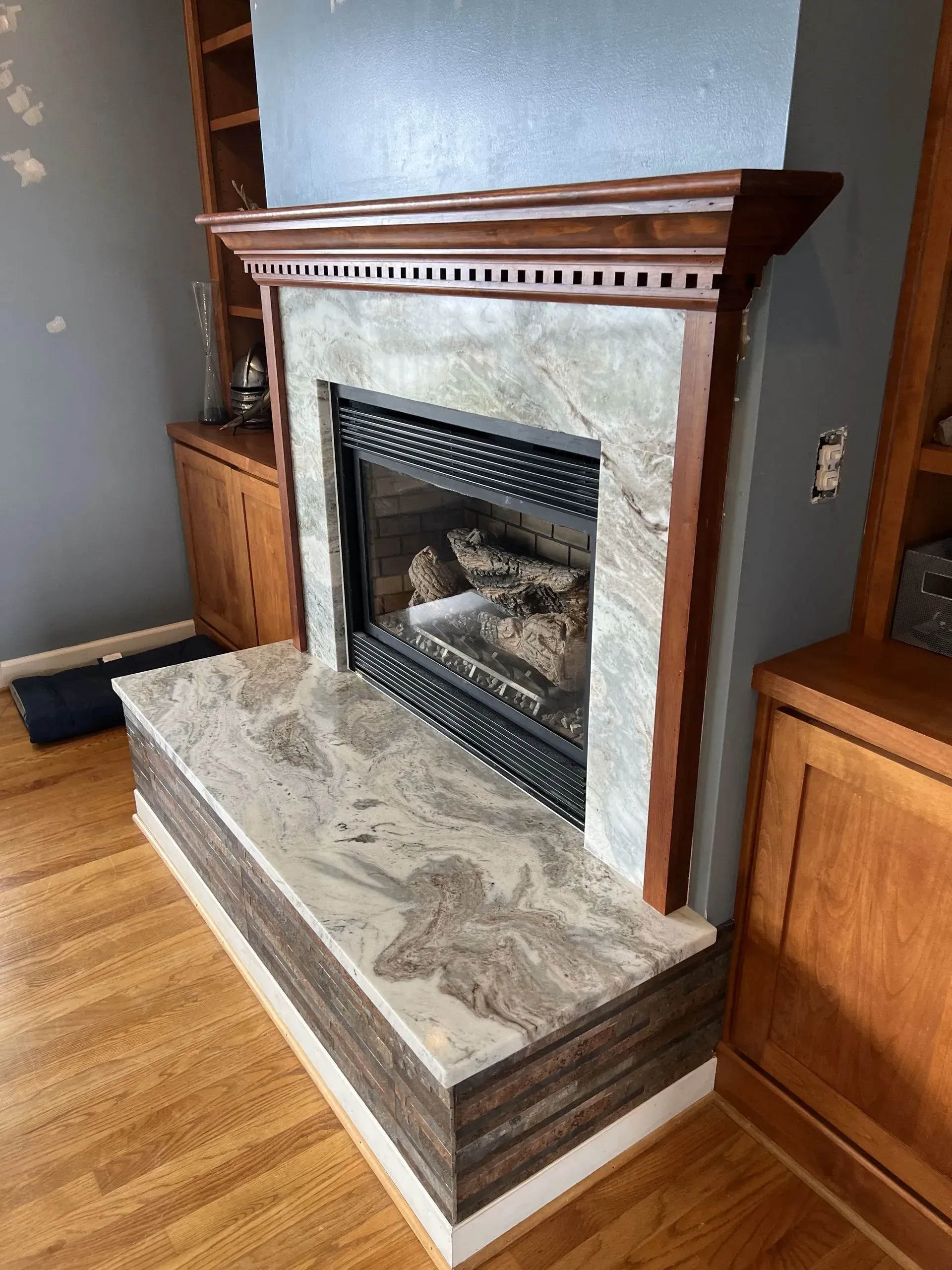 Fireplace with brown wooden mantle and gray marble surround, built-in cabinets on either side.