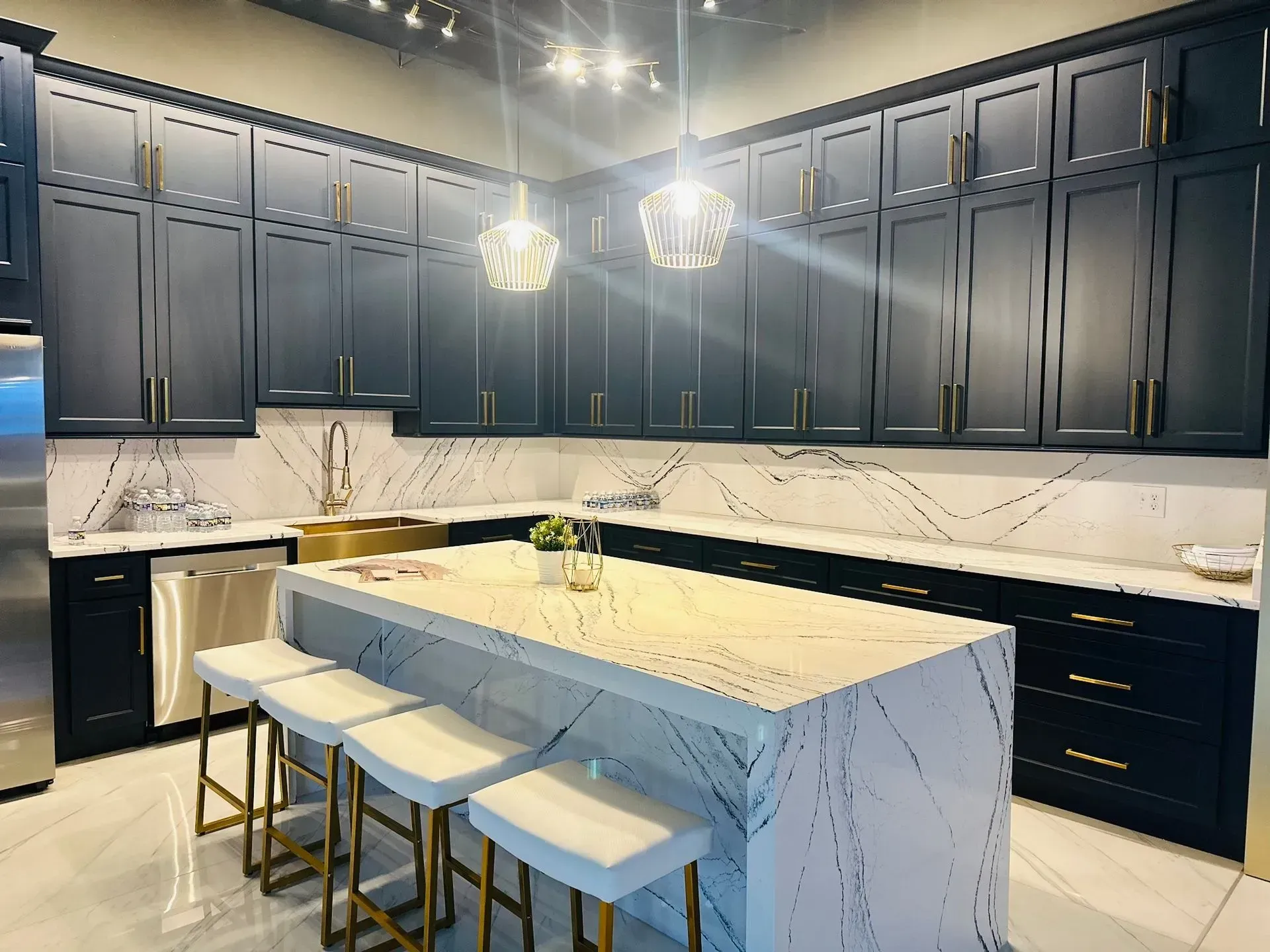 Dark blue kitchen with marble countertops, island with bar stools, and gold hardware.