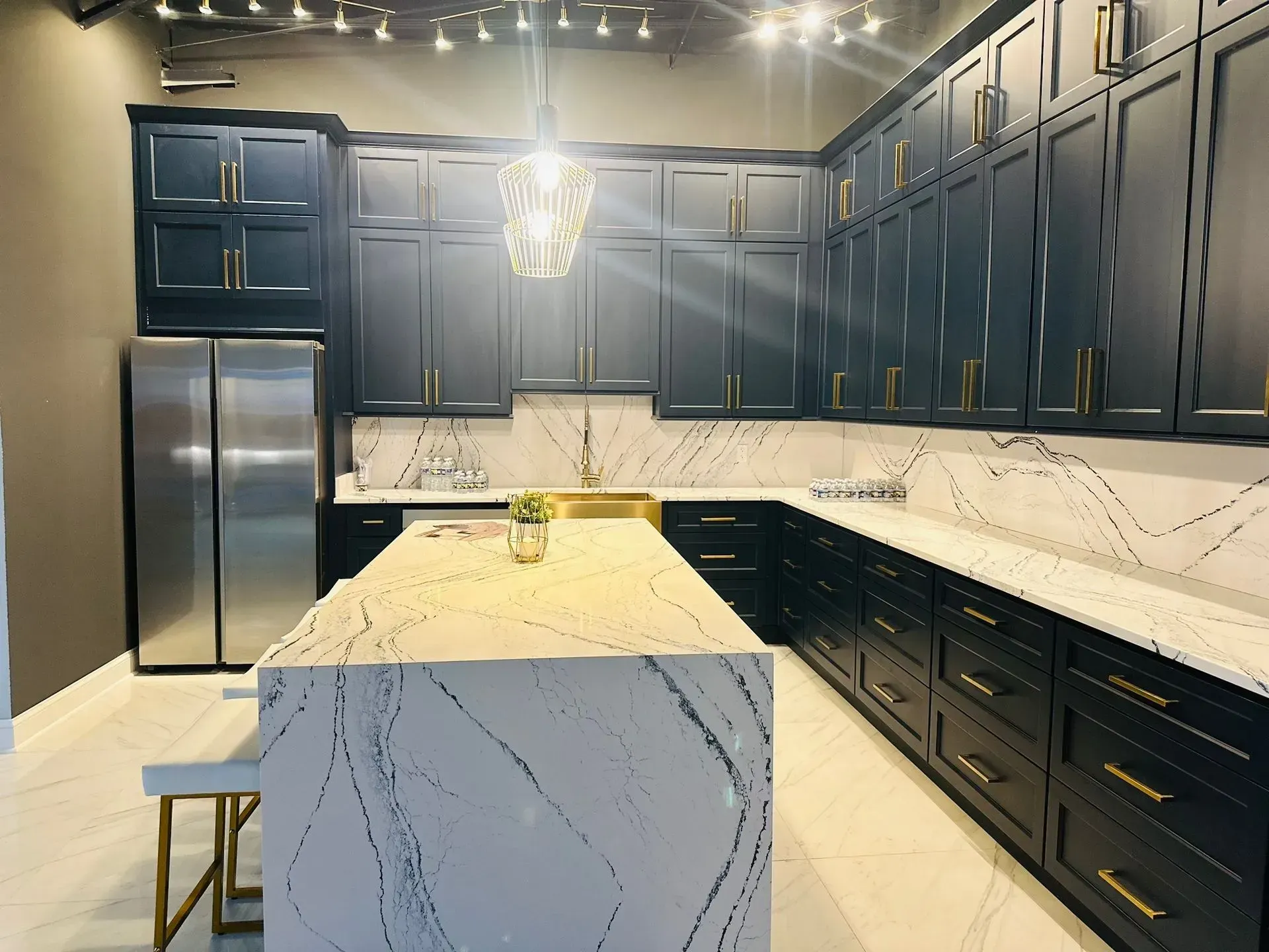 Modern kitchen with dark blue cabinets, gold hardware, white countertops, and stainless steel appliances.