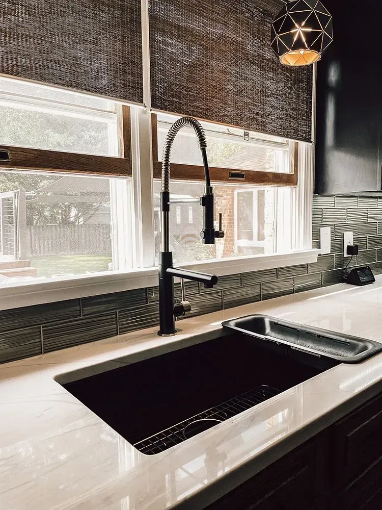 Modern kitchen sink with black faucet against a window, lit by a geometric pendant.