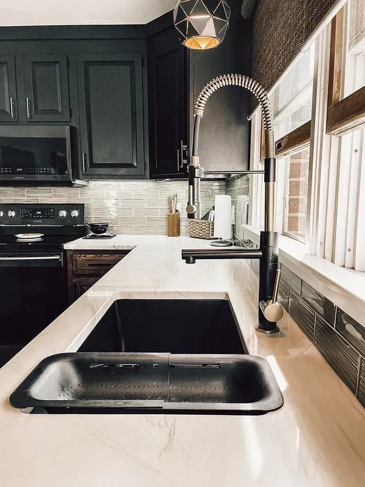 Modern kitchen with black cabinets, white countertop, and black sink; a window and faucet are visible.