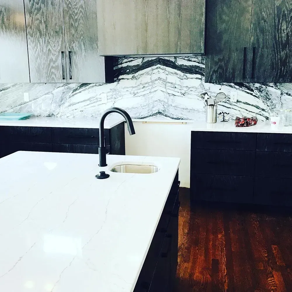 Modern kitchen with white countertop island, dark cabinets, and marble backsplash.