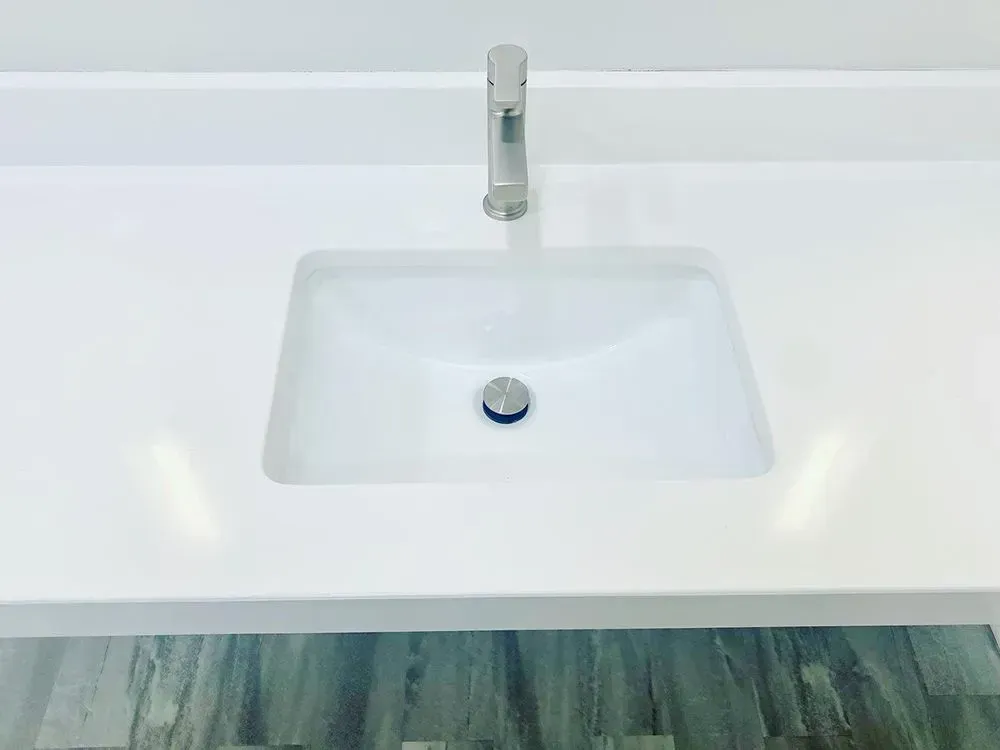 White bathroom sink and countertop with silver faucet against a grey floor.