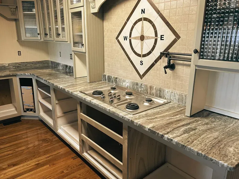 Kitchen with granite countertops, stovetop, compass backsplash, and light-colored cabinets.