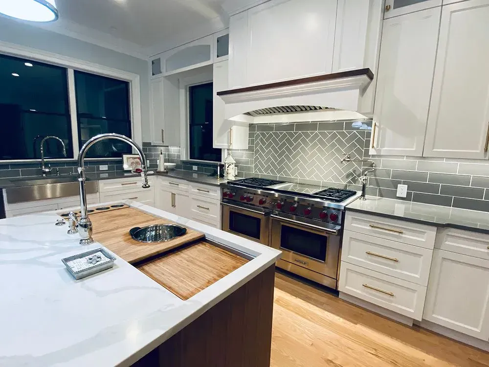 Modern kitchen with white cabinets, stainless steel appliances, and a gray herringbone backsplash.