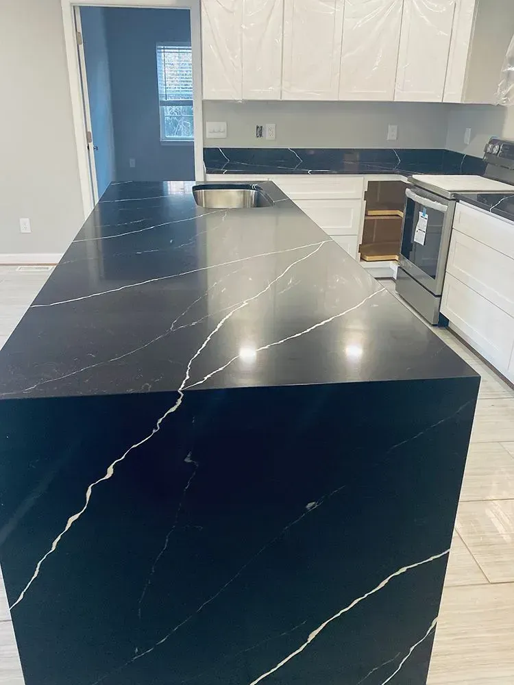 Black kitchen island with white veining, set in a kitchen with white cabinets and stainless steel appliances.