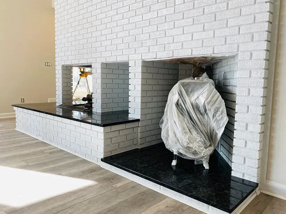 White brick fireplace with black granite hearth; equipment covered in plastic.