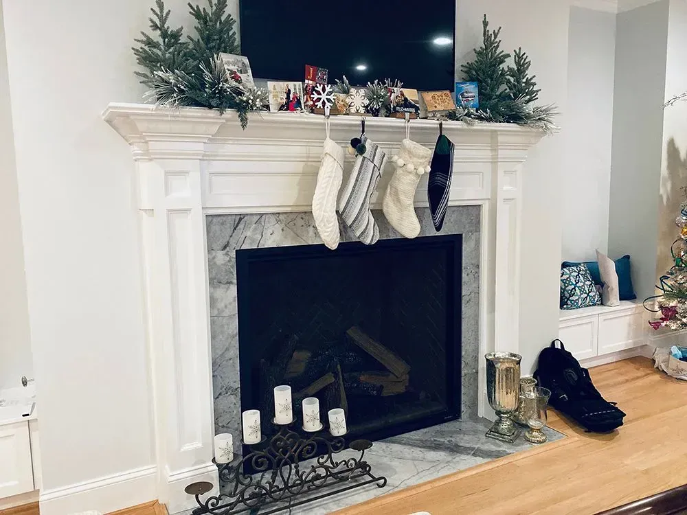 Christmas fireplace with stockings hanging from the mantel. Green garland, TV, and lit candles present.