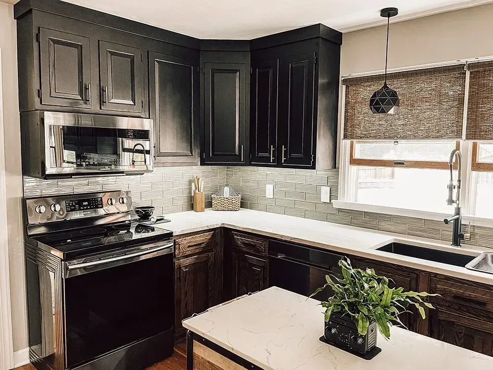 Dark kitchen with black cabinets, stainless steel appliances, and white countertops.