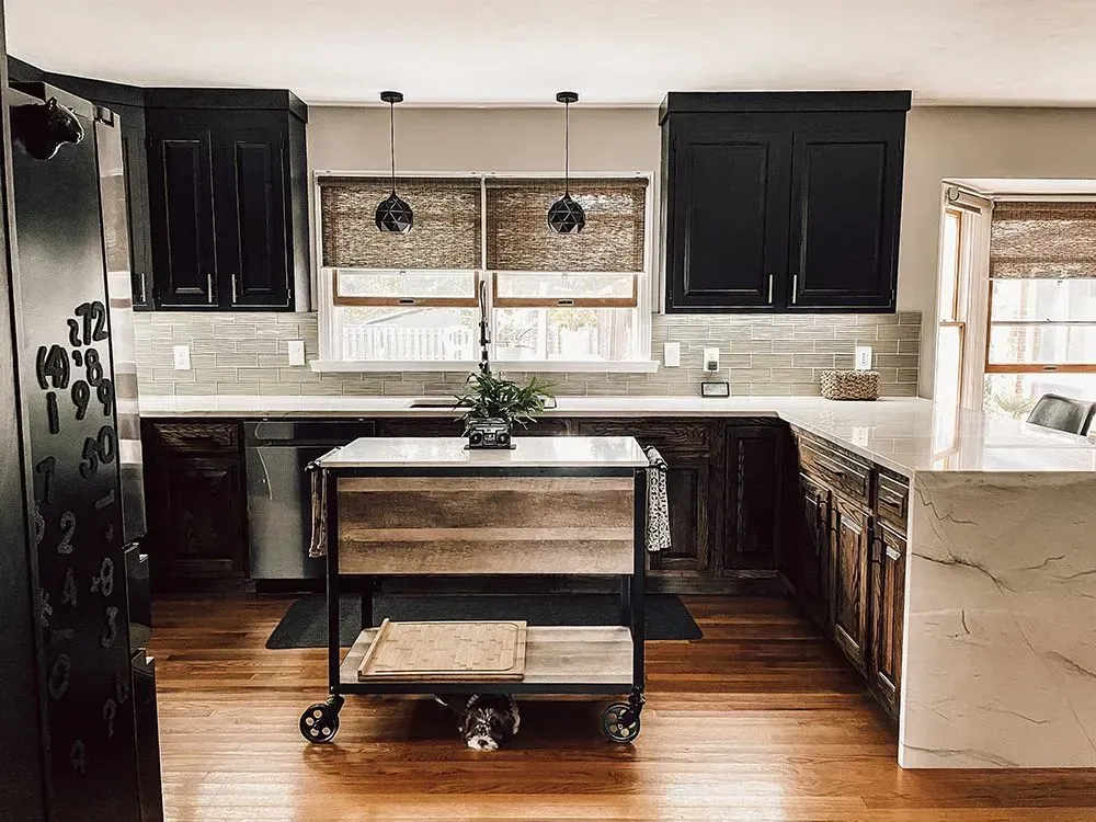 Kitchen with black cabinets, butcher block island on wheels, wood floors, and woven shades.