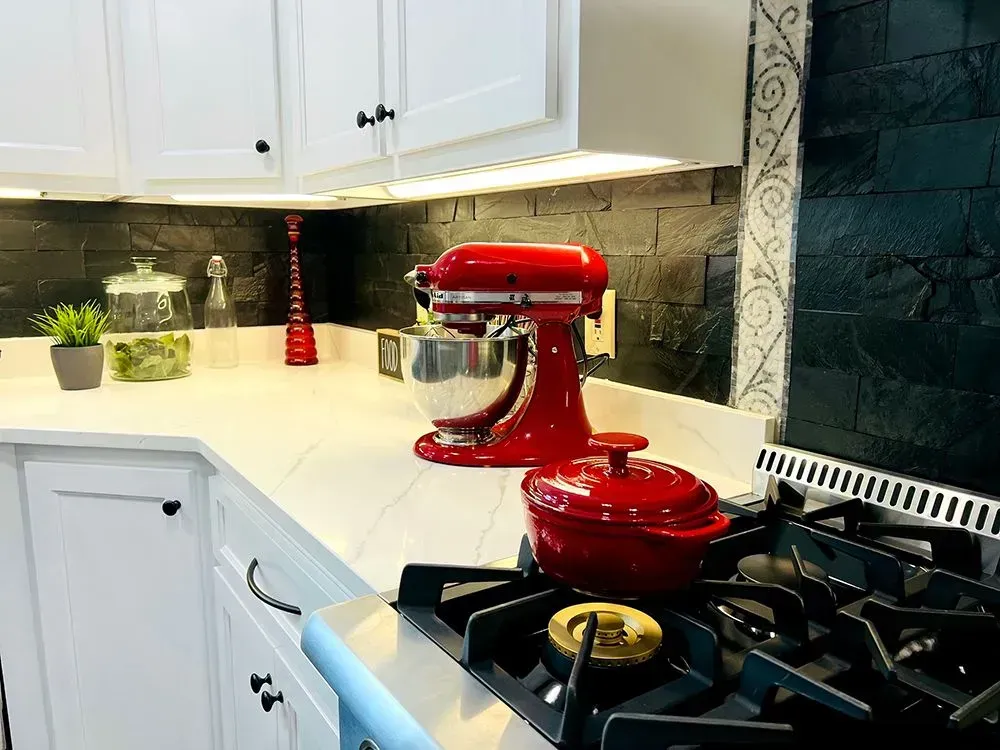 Kitchen countertop with a red stand mixer and a red pot next to a gas stove.