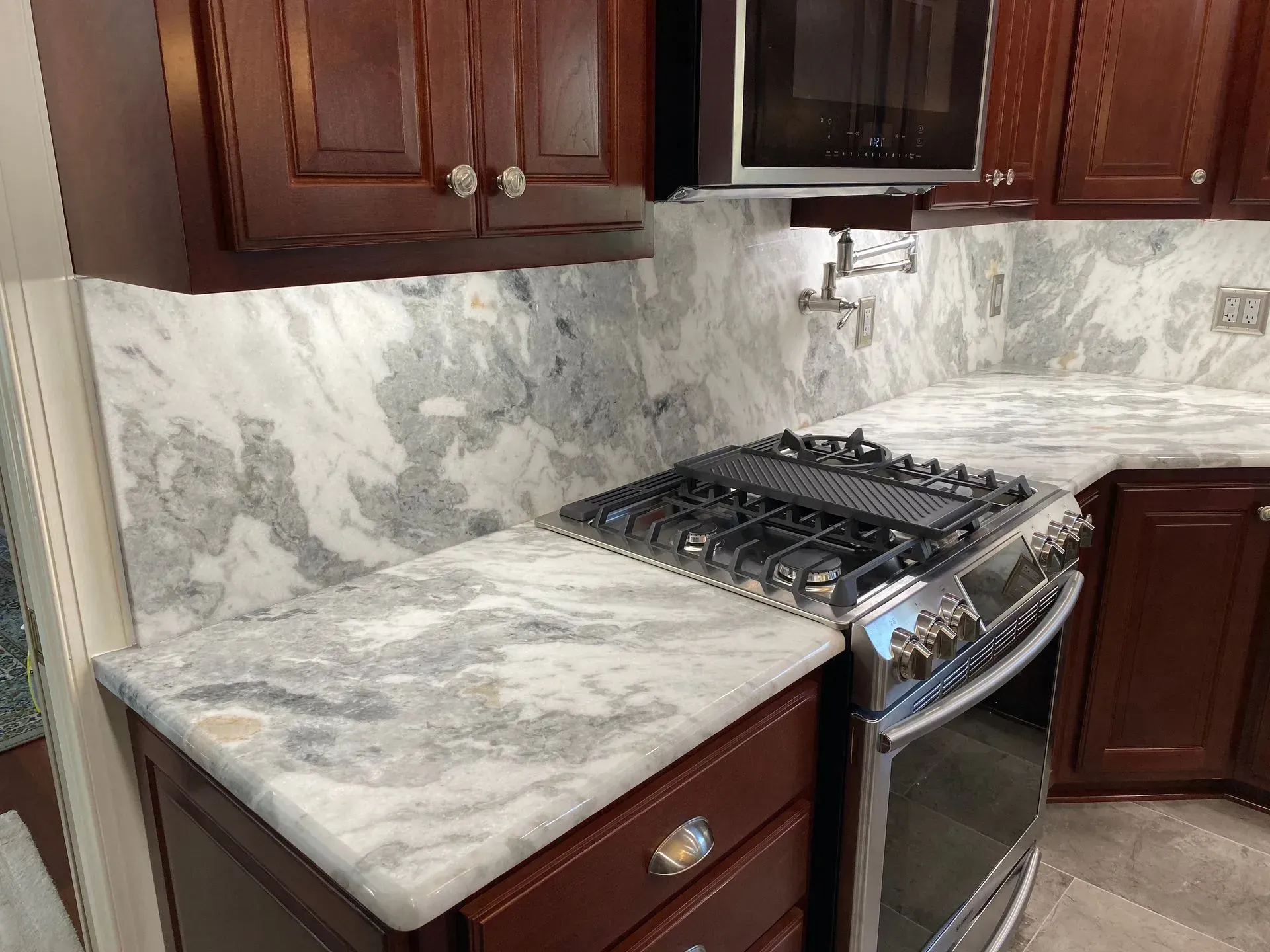 Kitchen with marble countertops, gas stove, and dark wood cabinets.