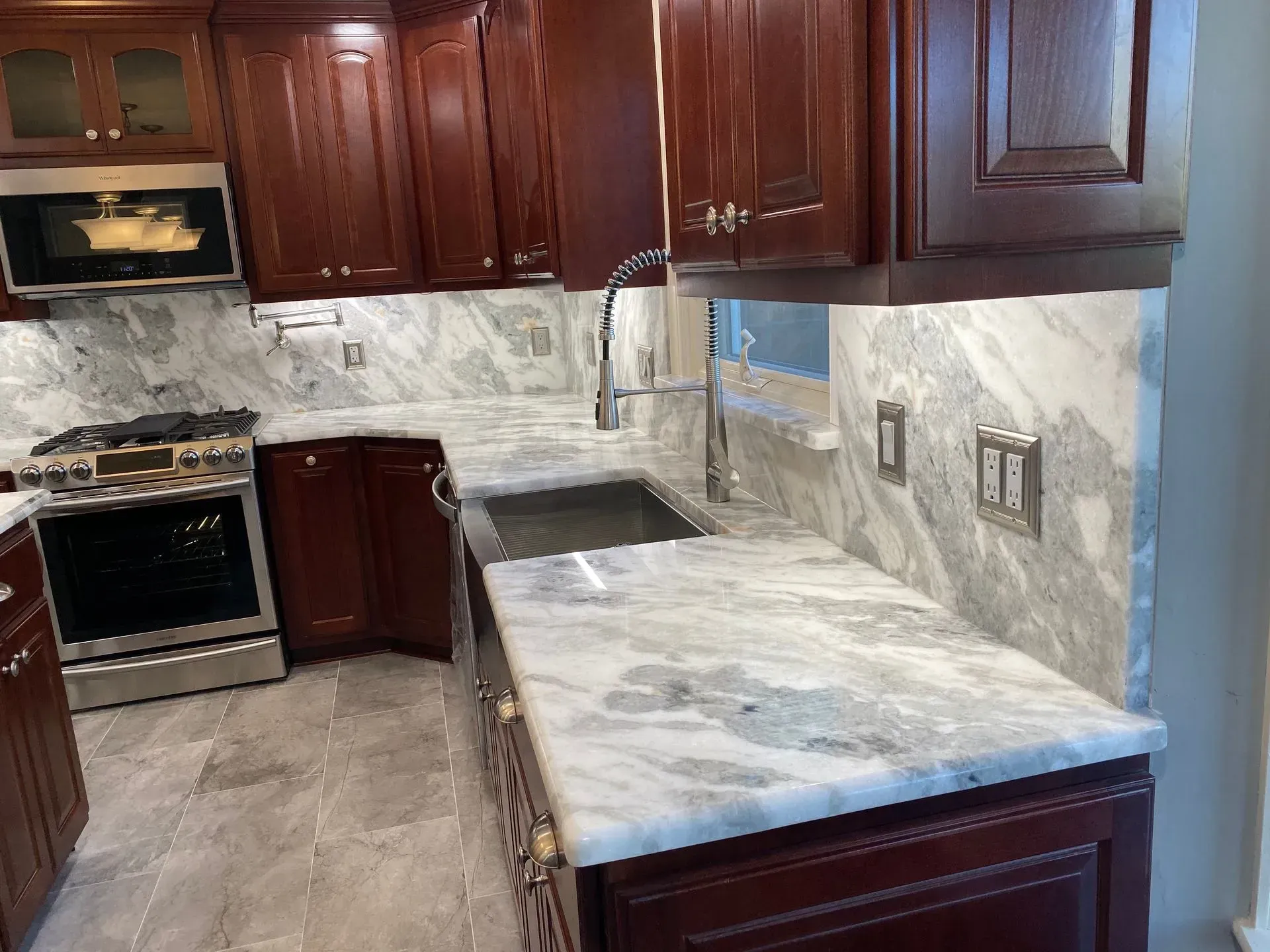 Dark wood kitchen cabinets with gray marble countertops and backsplash, stainless steel appliances.