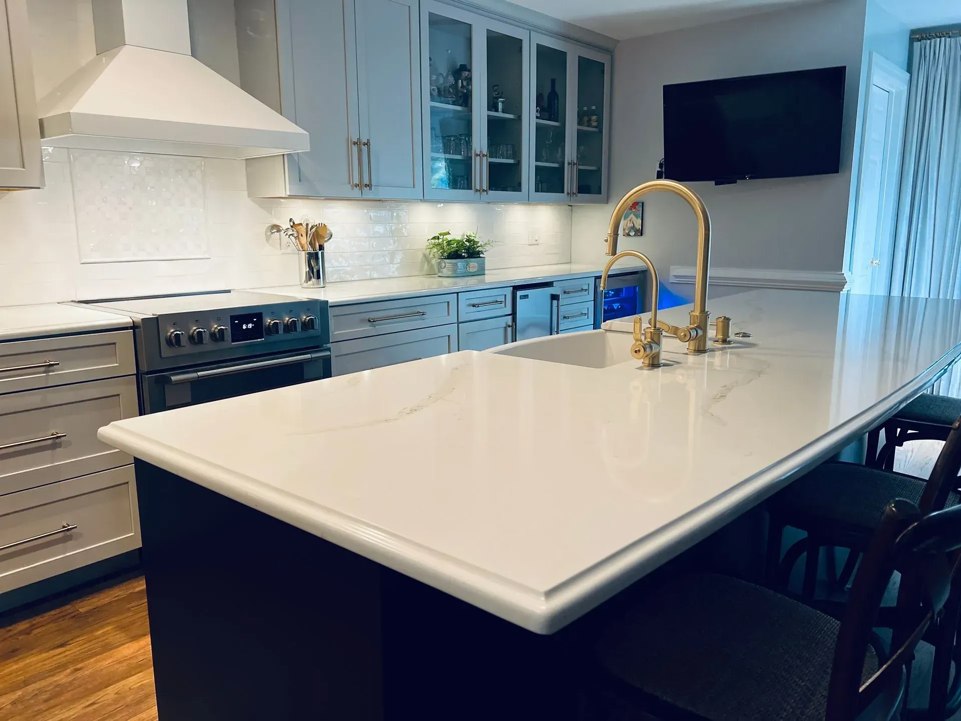 Modern kitchen with gray cabinets, white countertops, island with a sink, and gold faucet.