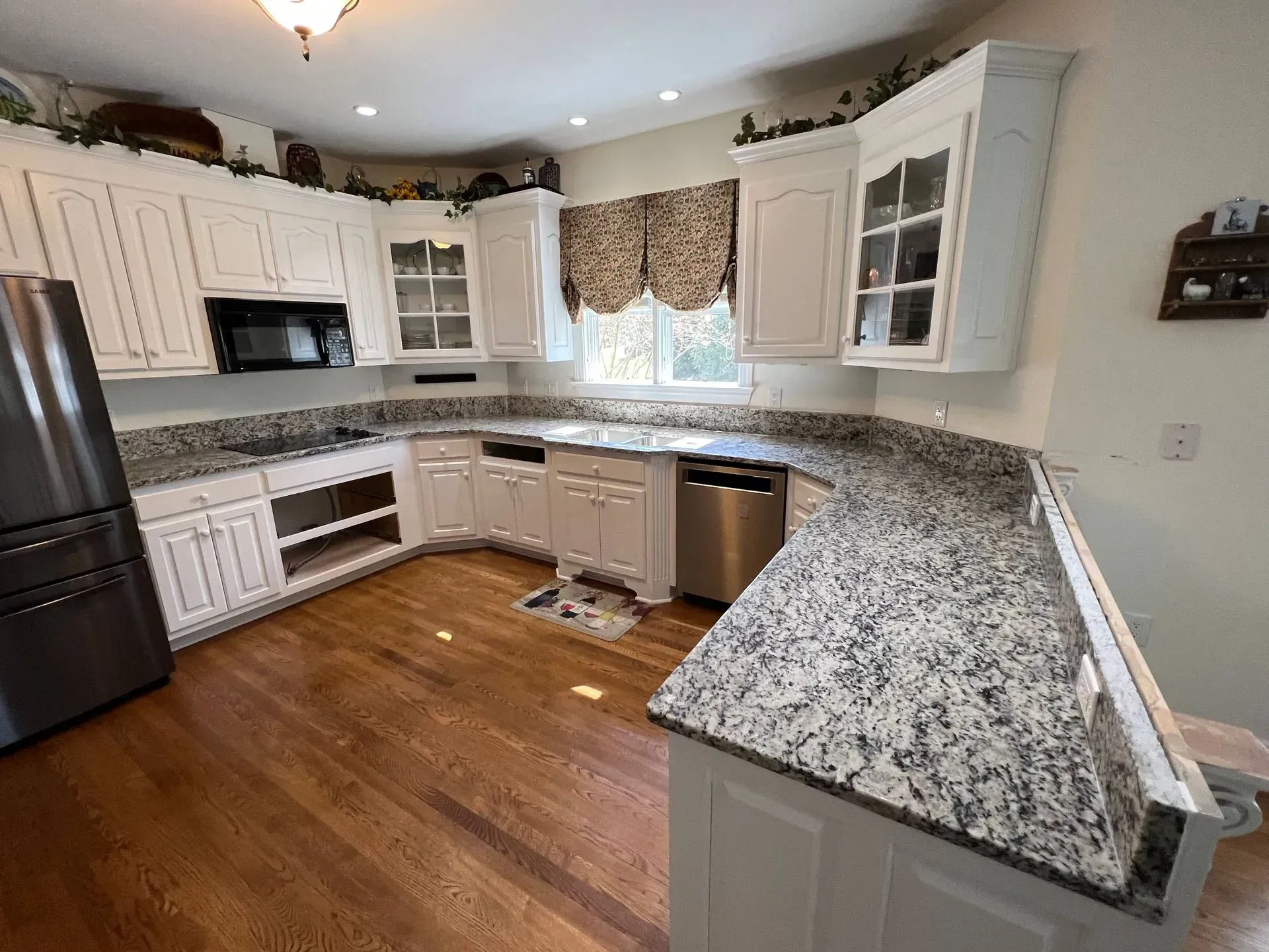 White kitchen with granite countertops, stainless steel appliances, and wood flooring.