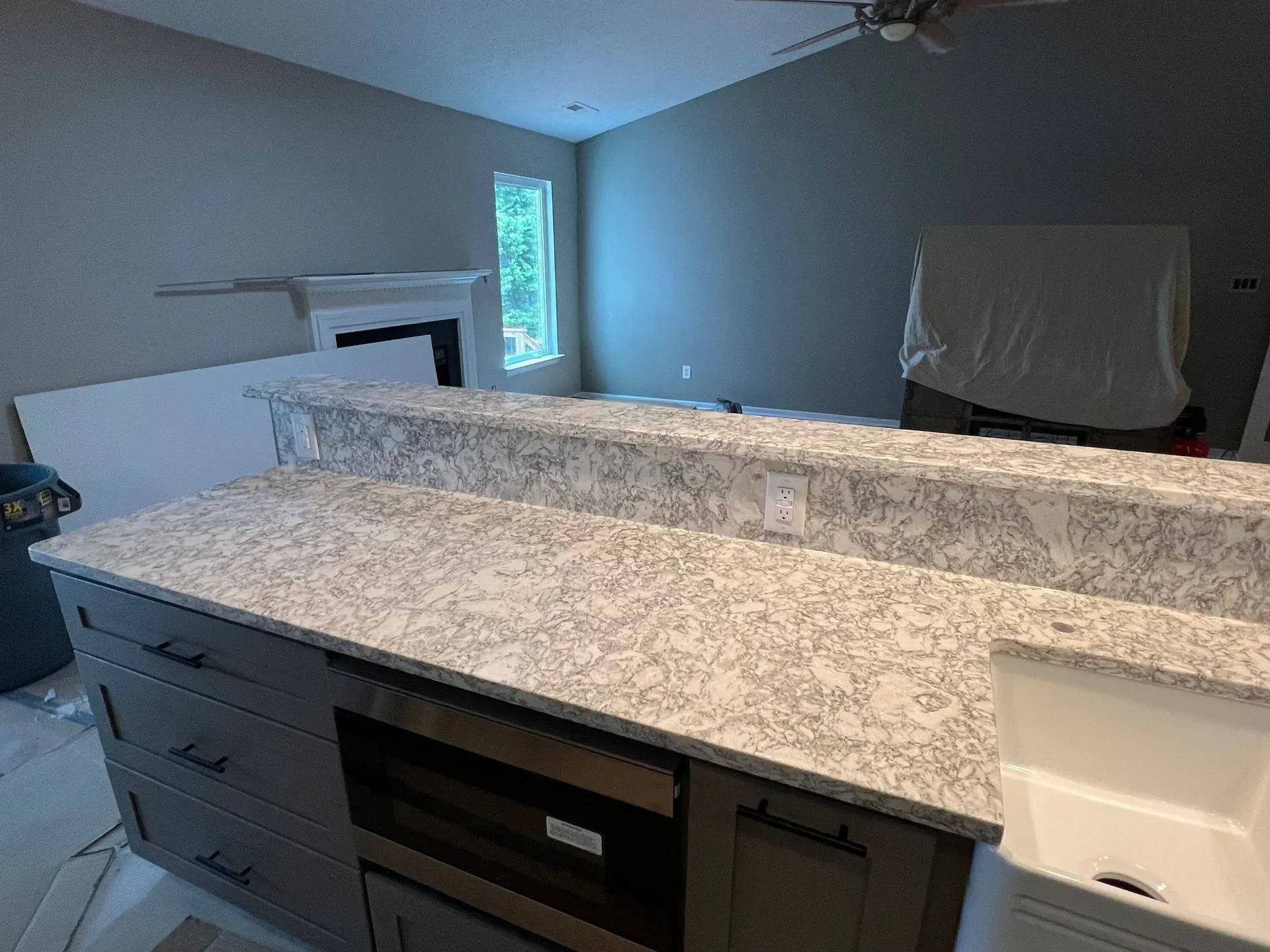 Kitchen island with gray cabinets and speckled countertops, built-in microwave, and sink.