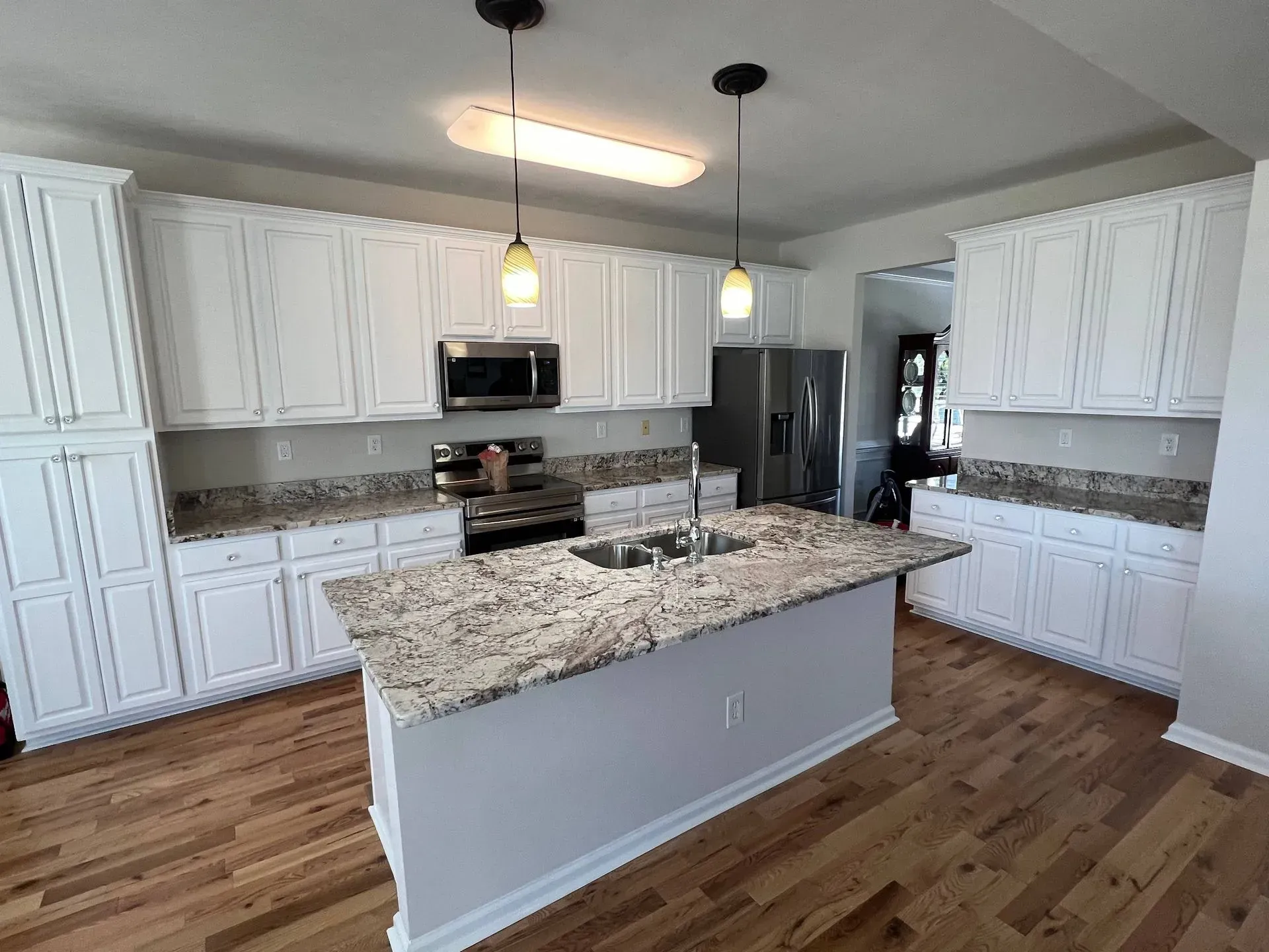White kitchen with island, cabinets, granite countertops, stainless steel appliances, and hardwood floors.