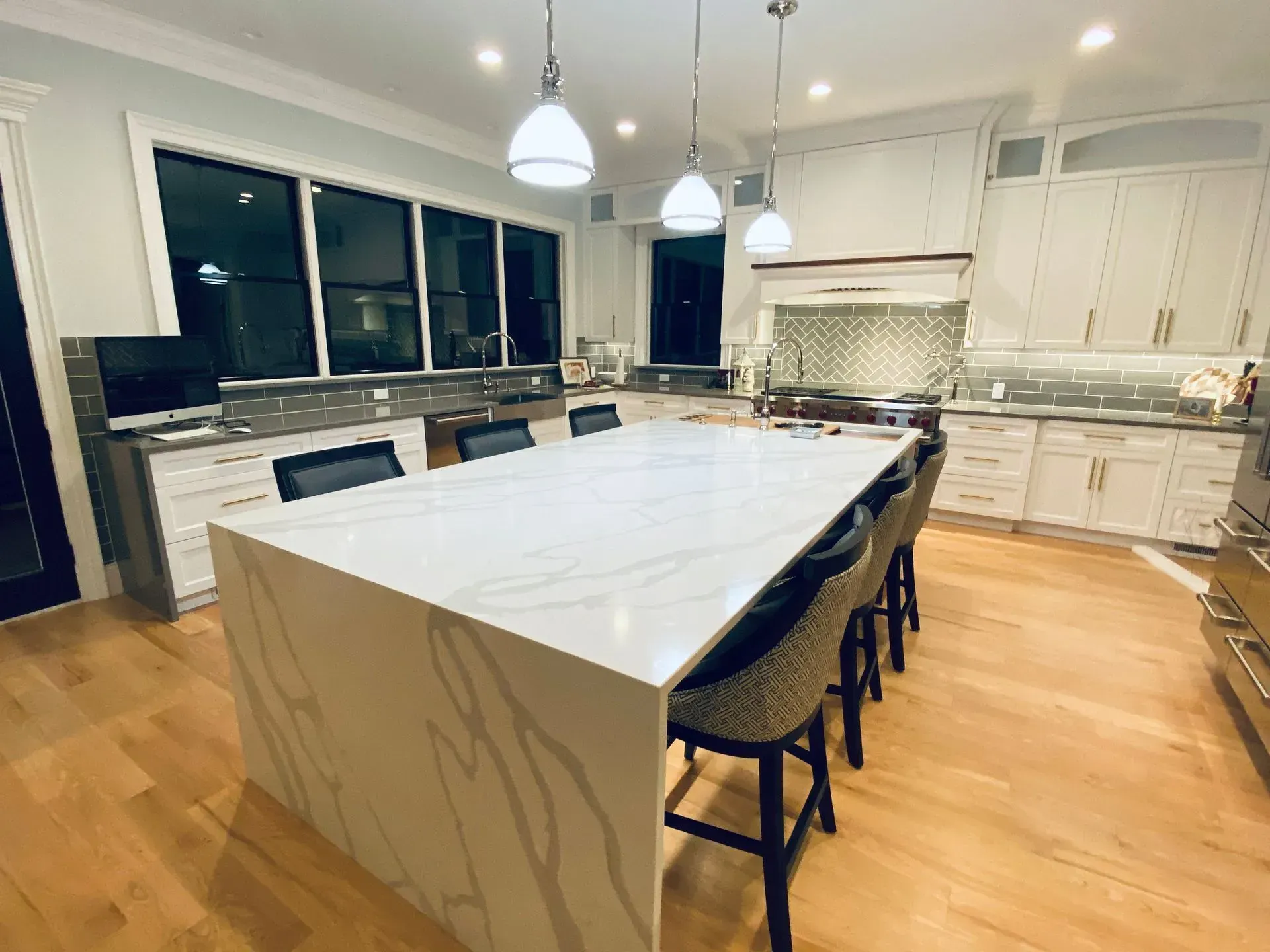 Modern kitchen with a large white countertop island, pendant lights, and hardwood floors.