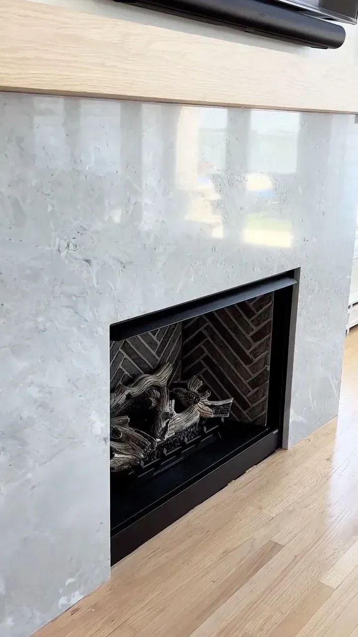 A fireplace with a marble-like facade and a black firebox. The surround has a light wood mantle.