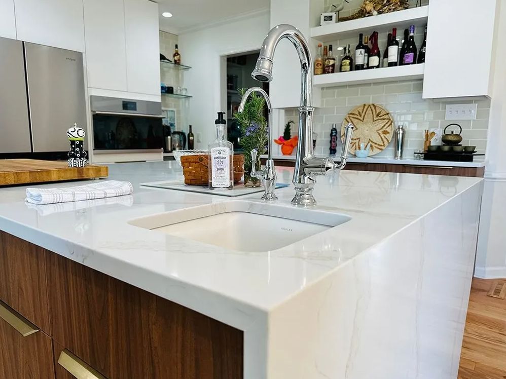 Modern kitchen island with white countertop and sink, dark wood cabinets, and chrome faucet.
