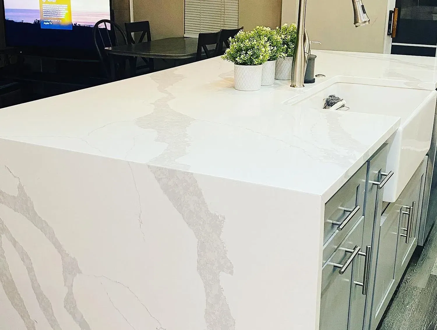 Kitchen island with a white countertop and grey veining, sink, cabinets, and decorative plants.