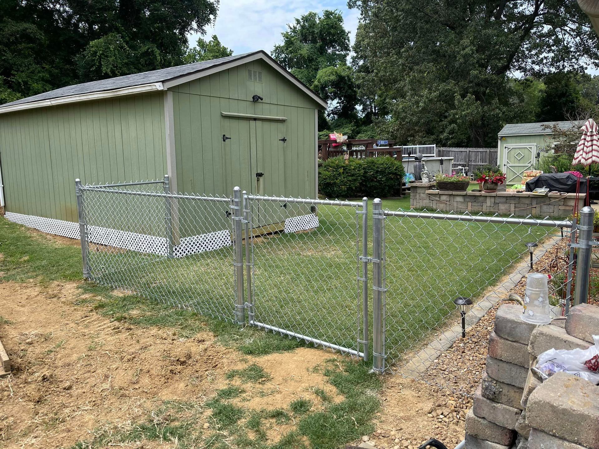A chain link fence is surrounding a green shed in a backyard