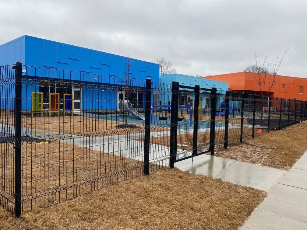 A black fence surrounds a playground in front of a blue building.