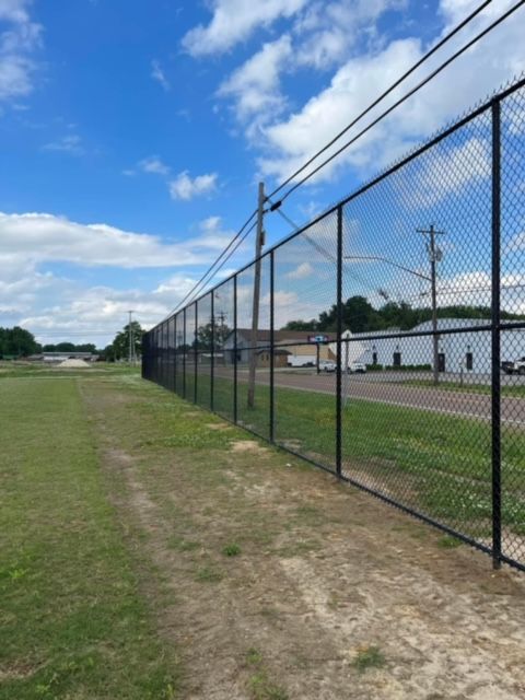 A chain link fence surrounds a grassy field on a sunny day