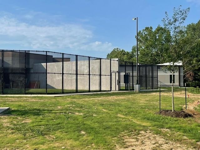 A large building with a fence around it is surrounded by grass and trees