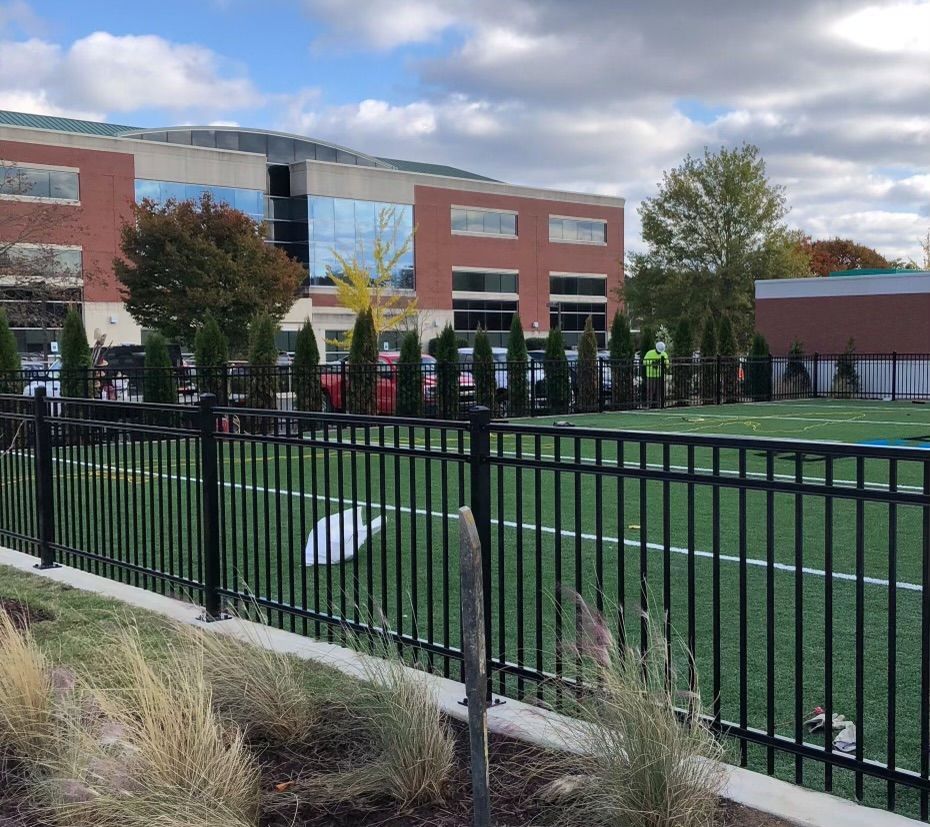 A fence surrounds a soccer field with a large building in the background